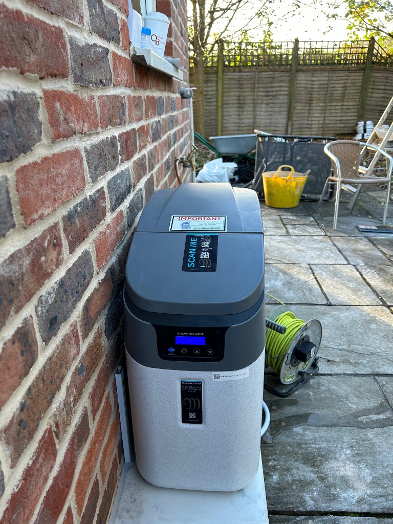 Whole-house water softener installed outdoors on a level base, with neat copper pipework to the mains supply